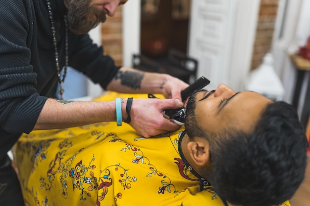 Jonge Indiaan in een kapperswinkel krijgt zijn baard geknipt door een kapper met een knipper