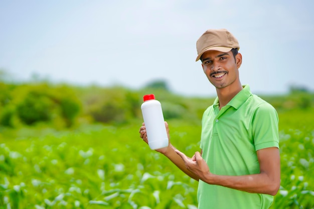 Jonge Indiase agronoom die een fles met vloeibare mest vasthoudt op een groen landbouwveld