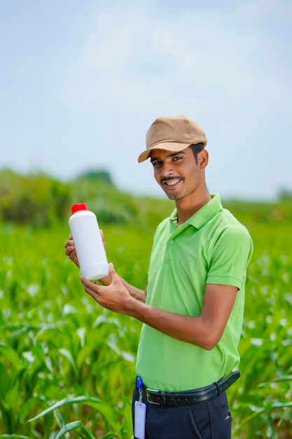 Jonge Indiase agronoom die een fles met vloeibare mest vasthoudt op een groen landbouwveld