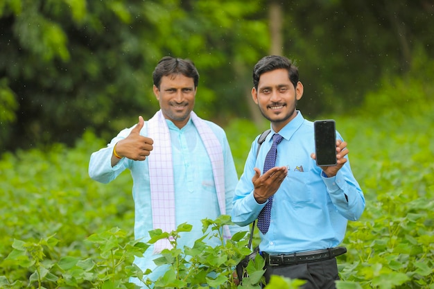 Jonge Indiase agronoom of bankier die smartphone met boeren toont op landbouwgebied.