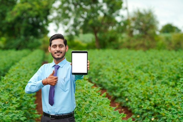 Jonge Indiase agronoom of officier die tablet toont op landbouwgebied.