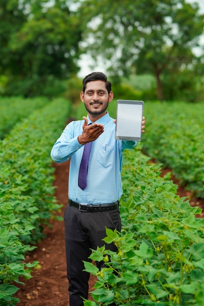 Jonge Indiase agronoom of officier die tablet toont op landbouwgebied.