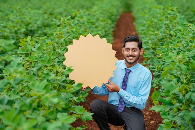 Jonge Indiase agronoom toont bord met kopieerruimte op landbouwveld.