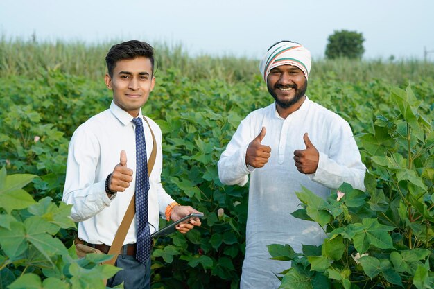 Foto jonge indiase agronoom toont wat informatie aan een boer in een tablet op een landbouwveld