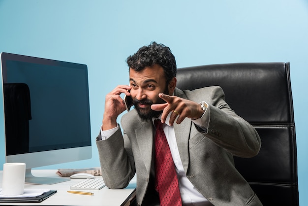 Jonge Indiase Aziatische zakenman in baard bezig met telefoongesprek tijdens het gebruik van laptop of computer op kantoor