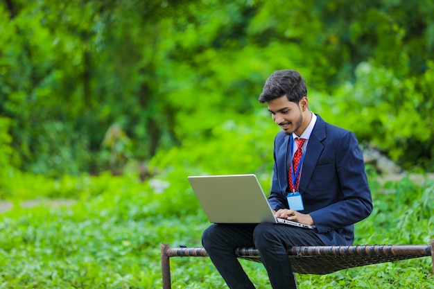 Jonge Indiase bankier met behulp van laptop op veld