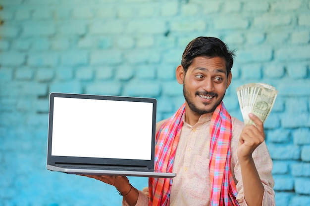 Jonge Indiase boer die laptopscherm en geld toont