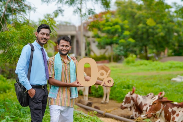 Jonge Indiase boer die nul procent symbool toont met agronoom of financier op zijn veeboerderij