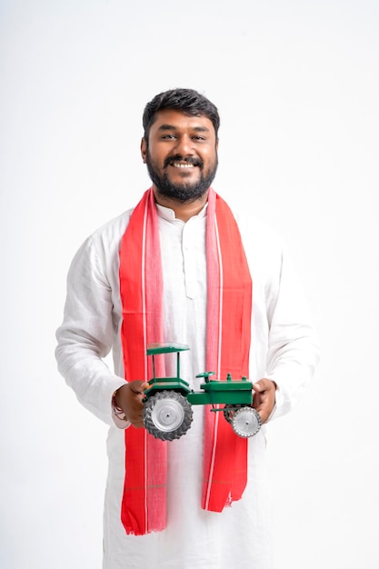 Jonge Indiase boer die tractor speelgoed toont op witte achtergrond