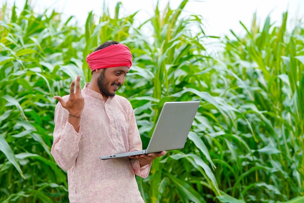 Jonge Indiase boer met behulp van laptop op landbouwveld.