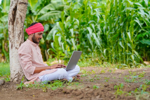 Jonge Indiase boer met behulp van laptop op landbouwveld.