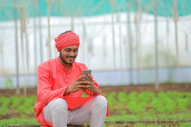 Jonge Indiase boer met behulp van slimme telefoon op kas