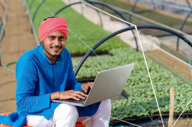 Jonge indiase boer met laptop op kas of poly huis