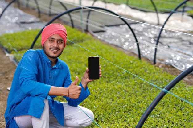 Jonge Indiase boer met slimme telefoon op poly huis of broeikasgassen