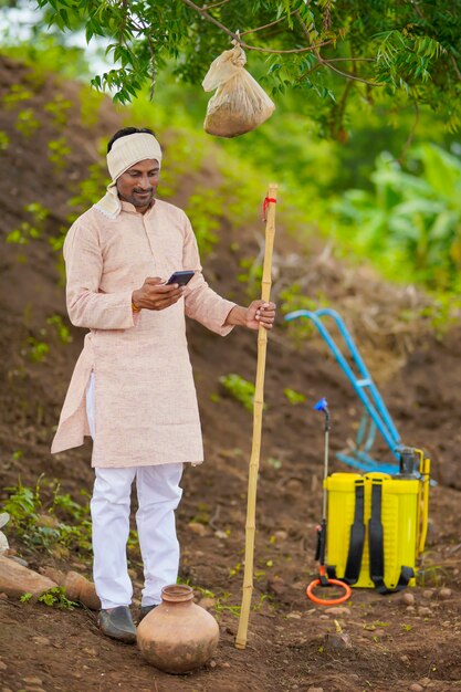 Jonge Indiase boer met smartphone op landbouwveld.