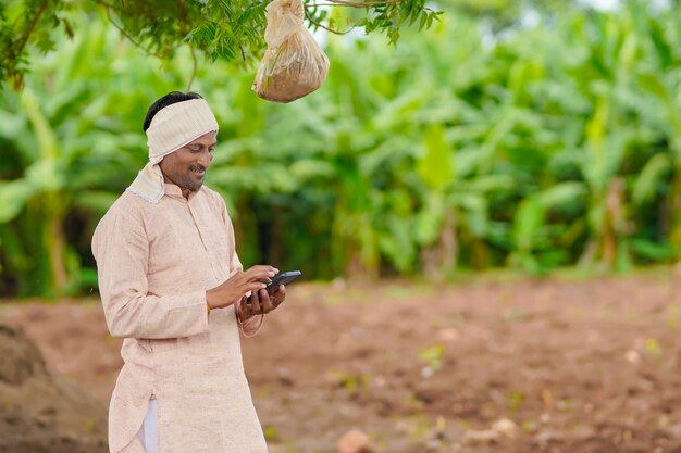 Jonge Indiase boer met smartphone op landbouwveld.