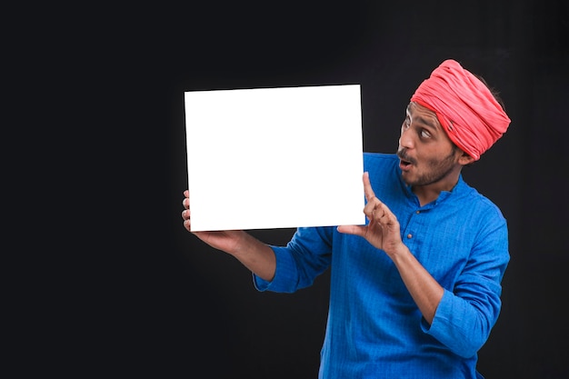 Jonge Indiase boer met wit karton op donkere achtergrond.