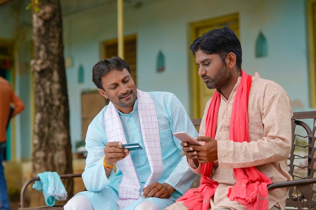 Jonge Indiase boeren die thuis een pinpas of creditcard met smartphone gebruiken