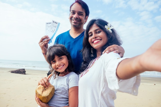Jonge Indiase familie ontspannen en selfie nemen op camera smartphone met ticket en kokosnoot in Goa