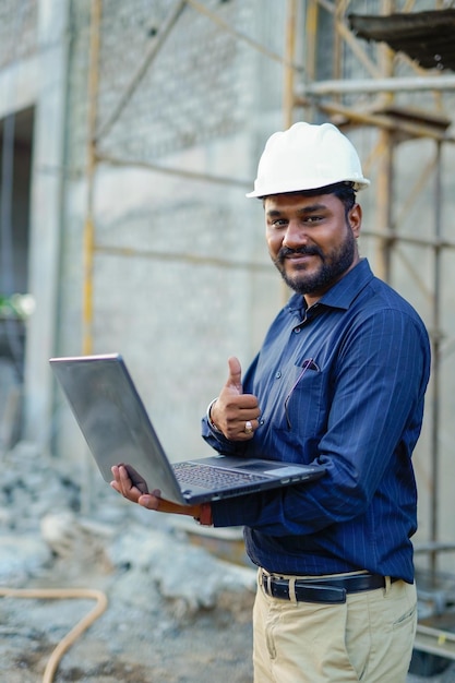 Jonge Indiase ingenieur in uniform en met behulp van laptop op veld