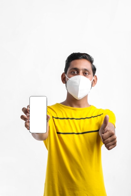 Jonge Indiase man die een masker draagt en een smartphone toont