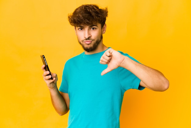 Jonge Indiase man met een telefoon met een afkeer gebaar, duimen naar beneden. Meningsverschil concept.