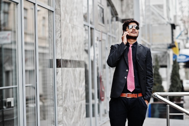 Jonge indiase man met stropdas en zonnebril poseerde buiten terwijl hij aan de telefoon sprak