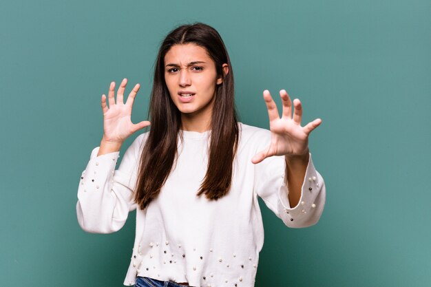 Jonge Indiase vrouw geïsoleerd op blauwe achtergrond boos schreeuwen met gespannen handen.