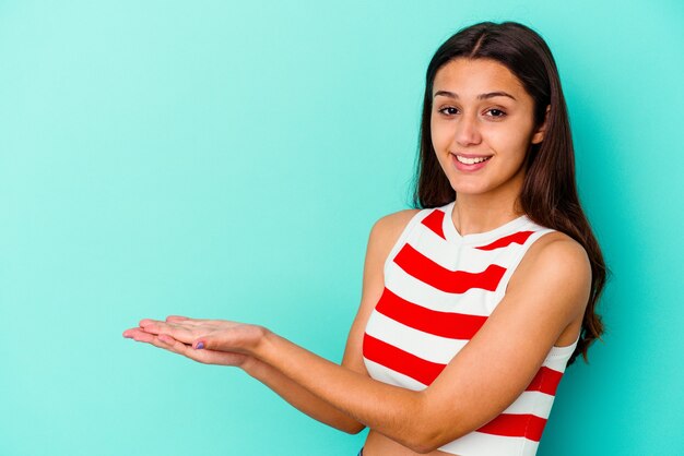 Jonge Indiase vrouw geïsoleerd op blauwe muur met een kopie ruimte op een palm.