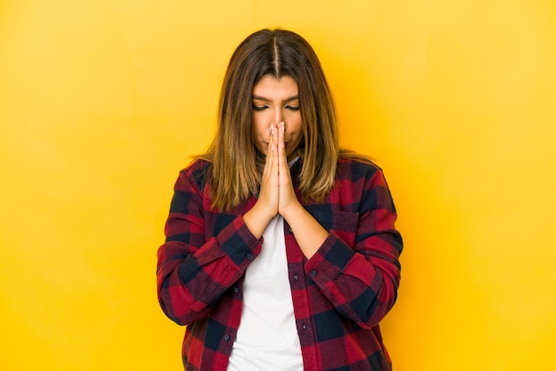 Jonge Indiase vrouw geïsoleerd op gele achtergrond bidden, toewijding, religieuze persoon op zoek naar goddelijke inspiratie.