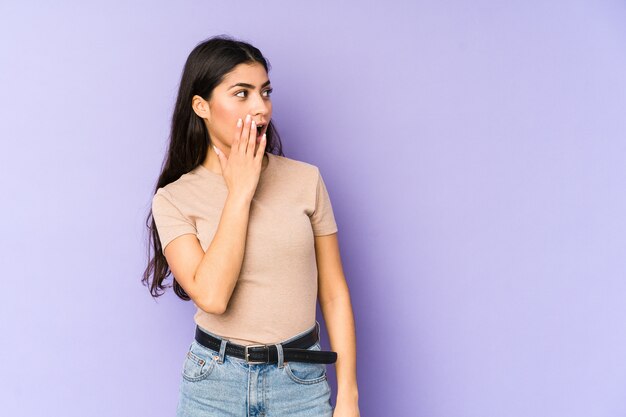 Jonge Indiase vrouw geïsoleerd op paarse muur geschokt vanwege iets dat ze heeft gezien.