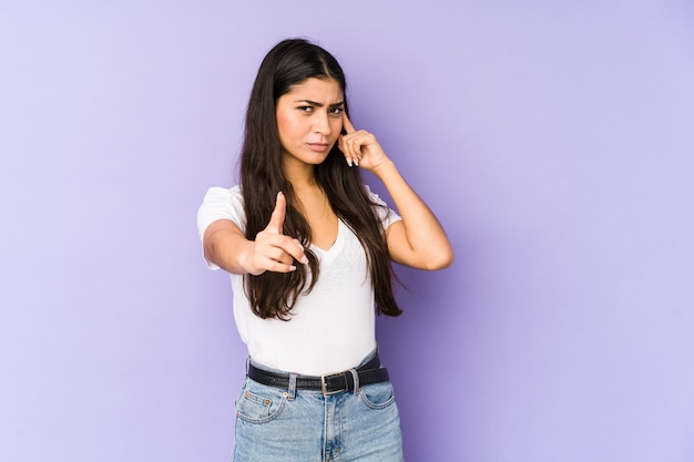 Jonge Indiase vrouw geïsoleerd op paarse muur wijzende tempel met vinger, denken, gericht op een taak.