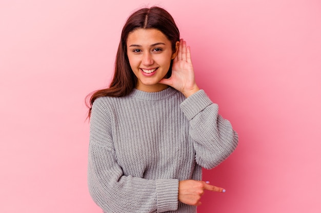 Jonge Indiase vrouw geïsoleerd op roze achtergrond proberen te luisteren een roddels.