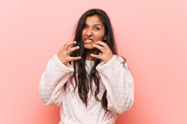 Jonge Indiase vrouw, gekleed in pyjama boos schreeuwen met gespannen handen.