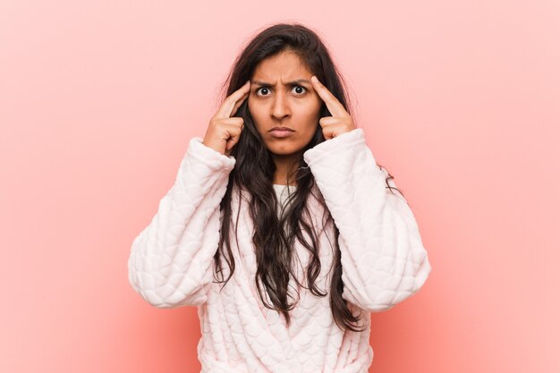 Jonge Indiase vrouw, gekleed in pyjama gericht op een taak, houdt hem wijsvingers hoofd hoofd.