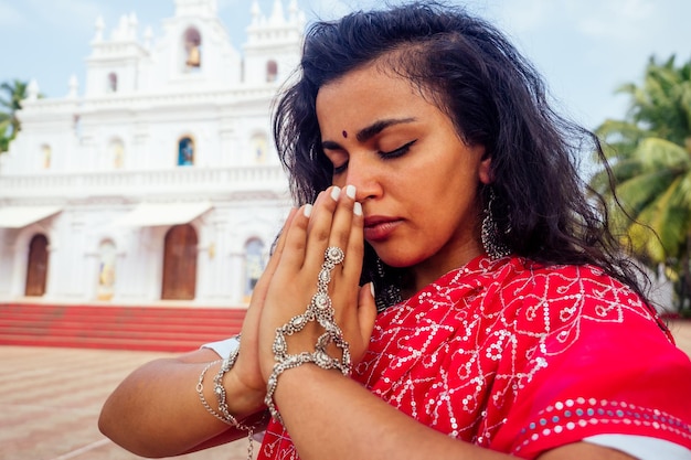 Jonge Indiase vrouw in traditionele sari rode jurk bidden in een hindoe tempel goa india Hinduismgirl uitvoeren van namaste gebaar katholicisme Delhi Street holi festivalom yoga meditatie vrouwelijk model