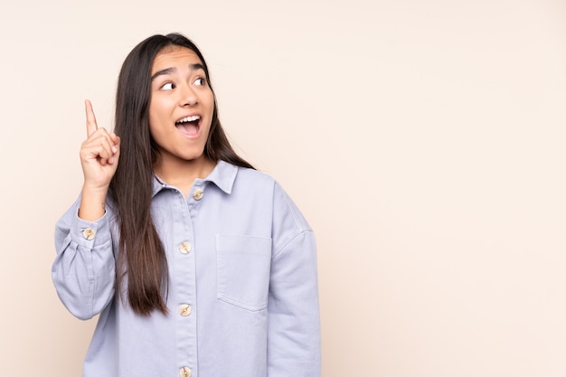 Jonge Indiase vrouw op beige muur van plan om de oplossing te realiseren terwijl het opheffen van een vinger