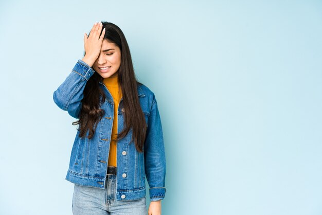 Jonge Indiase vrouw op blauw iets vergeten, voorhoofd met palm slaan en ogen sluiten.