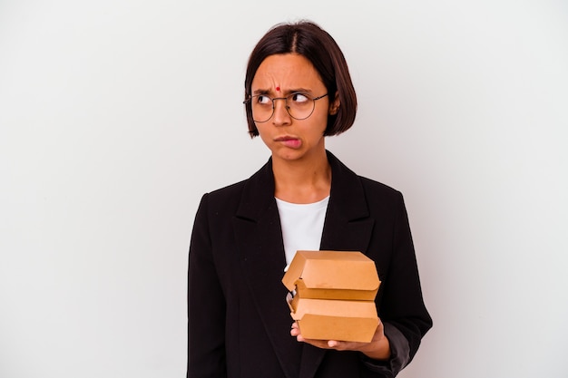 Jonge Indiase zakenvrouw eet hamburgers geïsoleerd verward, voelt twijfelachtig en onzeker.