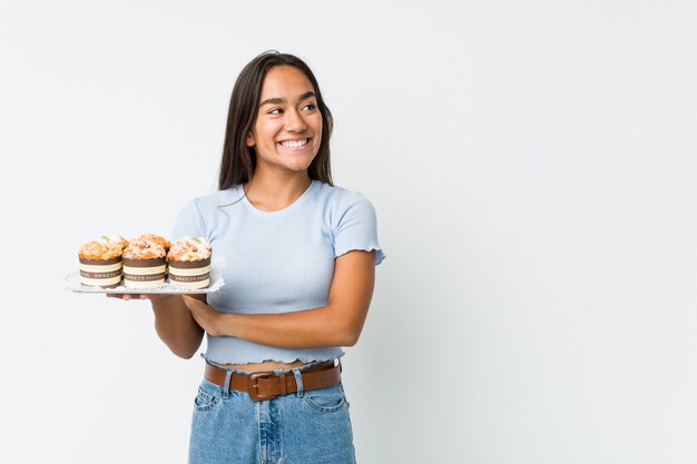 Jonge Indiër die zoete cakes glimlachen zeker met gekruiste wapens houden