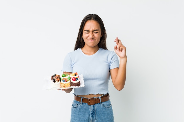 Jonge Indiër die zoete cakes houden die vingers kruisen voor het hebben van geluk