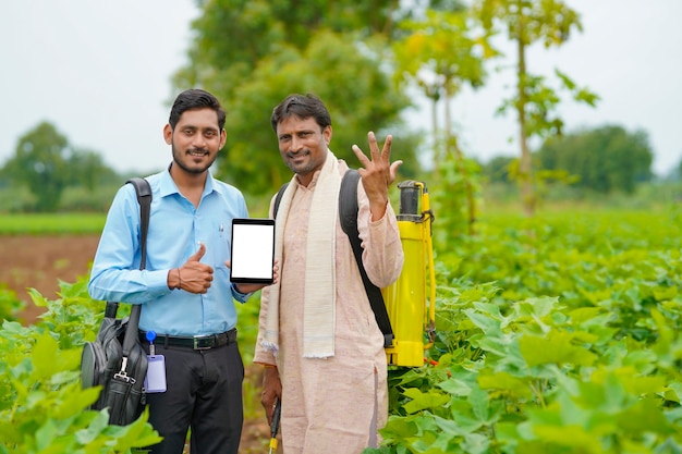 Jonge indische agronoom of bankier die tablet met landbouwer toont bij landbouwgebied.