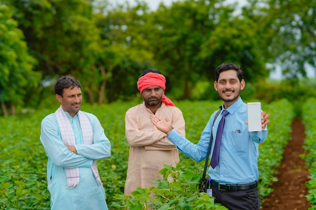 Jonge indische agronoom of bankier die tablet met landbouwers toont bij landbouwgebied.