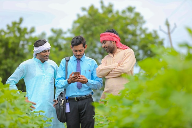 Jonge indische agronoom of bankier die wat informatie toont aan boer in smartphone op landbouwgebied.