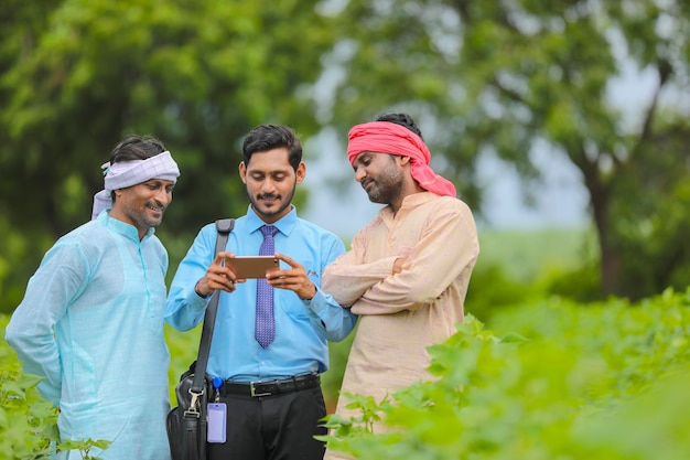 Jonge indische agronoom of bankier die wat informatie toont aan boer in smartphone op landbouwgebied.