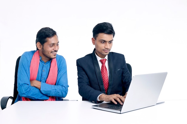 Jonge indische bankier die wat informatie geeft aan boer op laptop op kantoor.