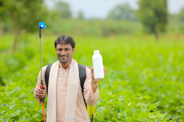 Jonge indische boer die vloeibare meststoffles toont bij landbouwgebied.