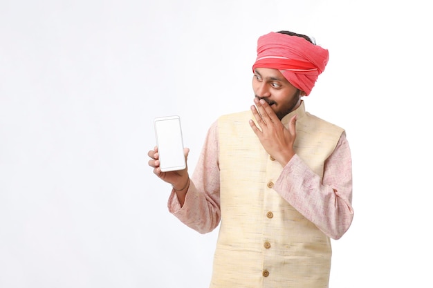 Jonge indische man die smartphone toont en uitdrukking geeft op witte achtergrond.