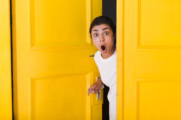 Foto jonge indische vrouw die door gele deur gluurt.