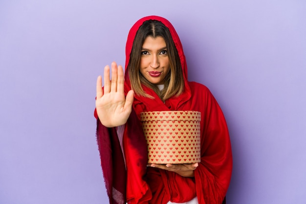 Jonge indische vrouw die een hijab draagt die een geïsoleerde gift van de valentijnskaartendag houdt status met uitgestrekte hand die stopbord toont, dat u verhindert.